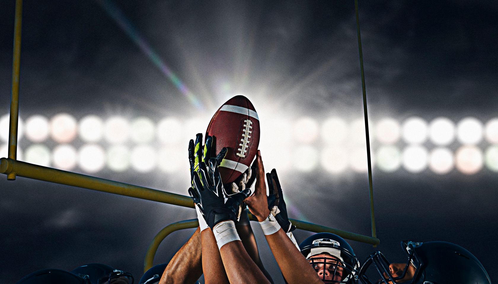 Victorious teenage and young male american football team holding up ball at night