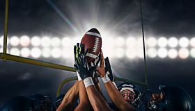 Victorious teenage and young male american football team holding up ball at night