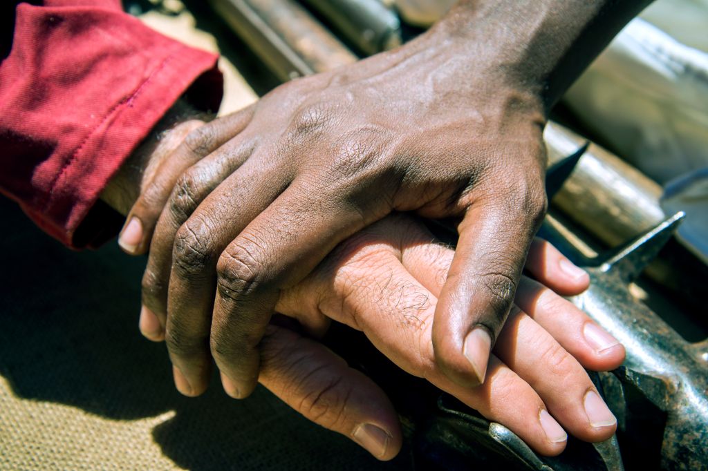 View of the hand of a Black man over the hand of a white man and rudimentary weapons