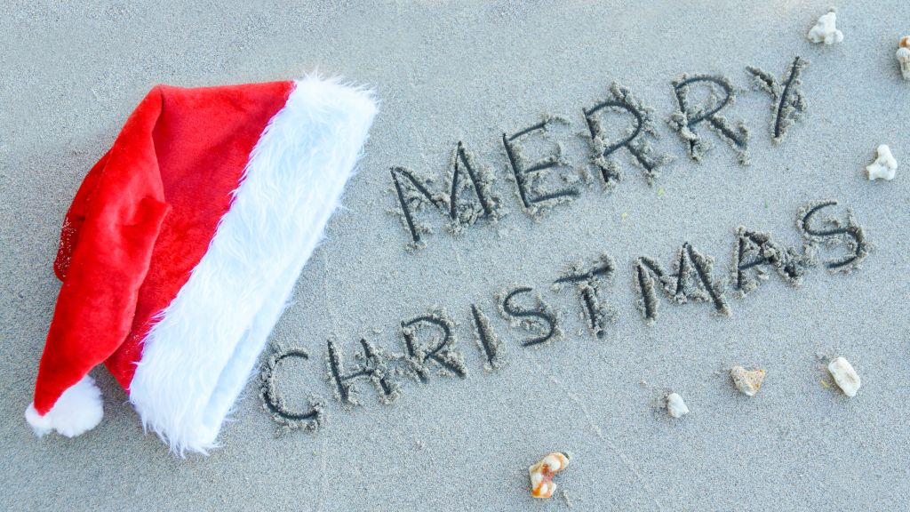 Words ''Merry Christmas'' written on sand at the beach and santa Hat