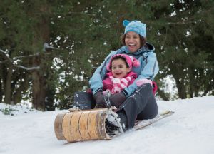 Mother and daughter sledding on snowy hill outdoors