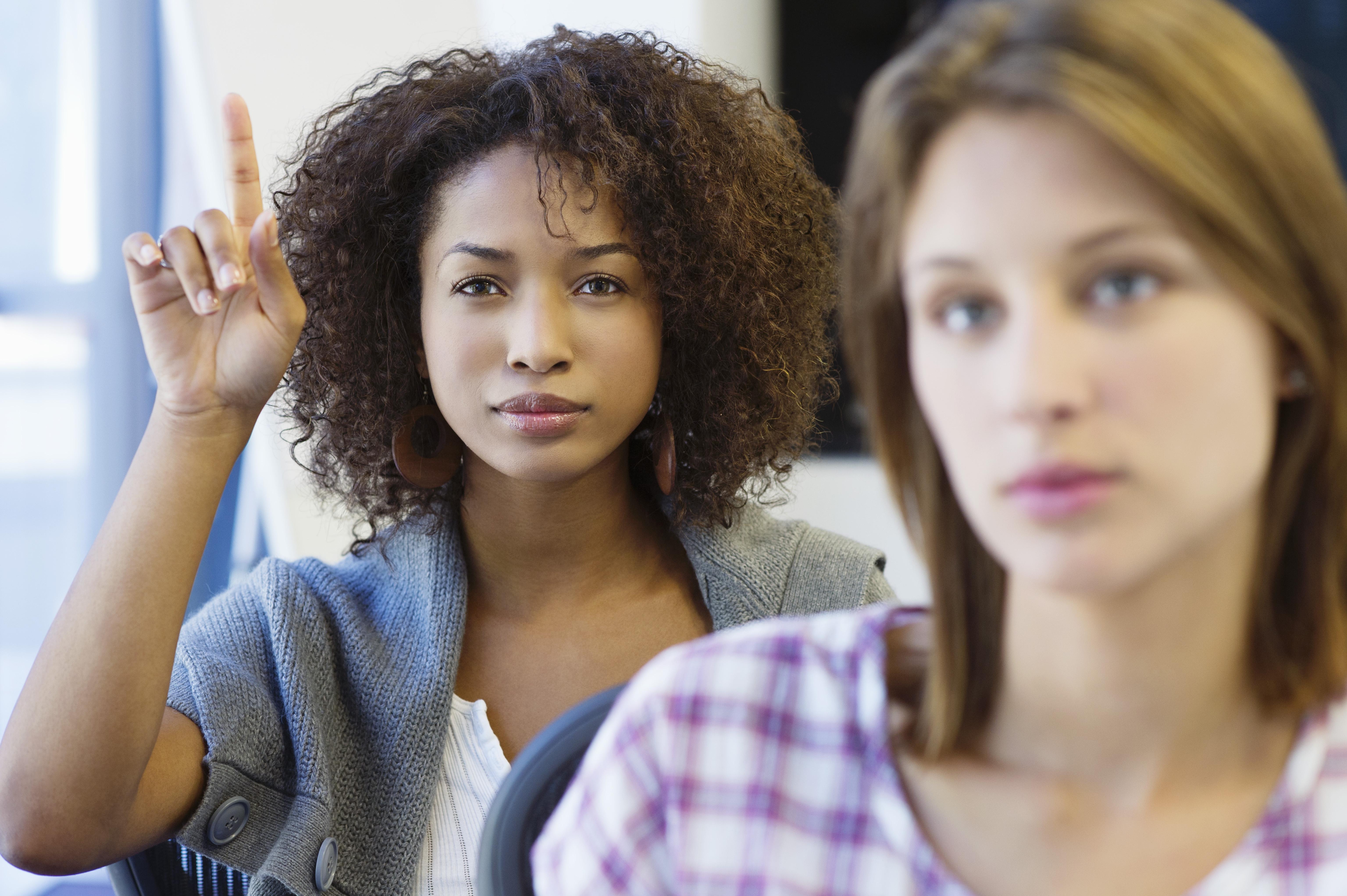 Two women sitting in classroom with focus on African American woman raising hand