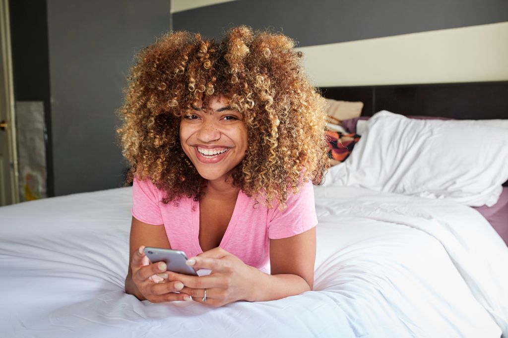 Smiling Black woman laying on bed texting on cell phone