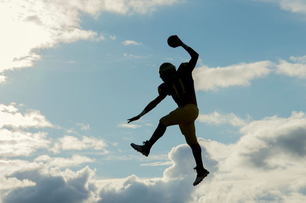Teenage american football player, jumping with ball, mid air