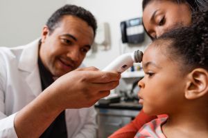 Mid adult doctor using medical equipment on young patient