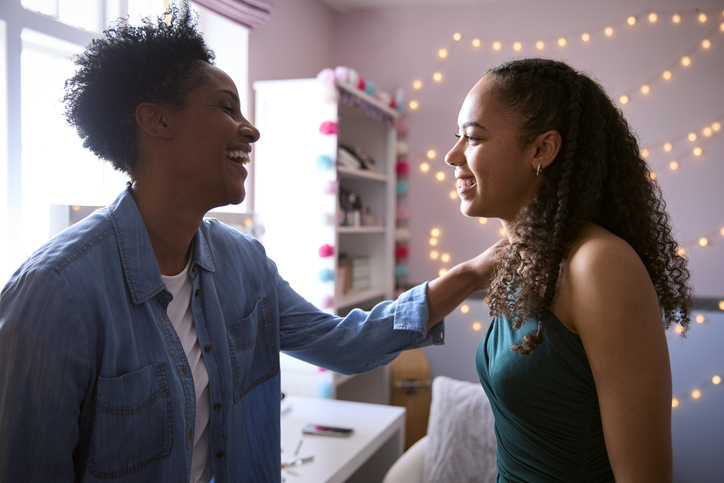 Mother Helping Teenage Daughter In Bedroom At Home Getting Ready For Prom Or Night Out