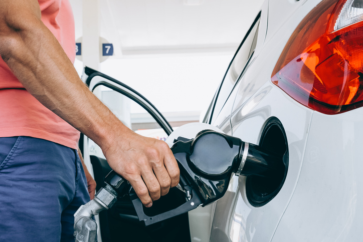Adult man hand holding fuel nozzle while filling gasoline into white car fuel tank. Close view of refueling process. Transportation energy consumption and automobile service concept.