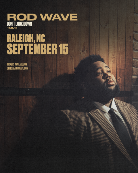 A man in a suit and tie sitting in a dimly lit room, with the text "ROD WAVE DON'T LOOK DOWN TOUR RALEIGH, NC SEPTEMBER 15" displayed prominently.