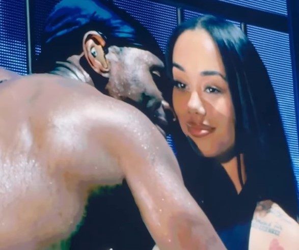 Two people, a shirtless man and a woman in a black top, embracing in an intimate pose.